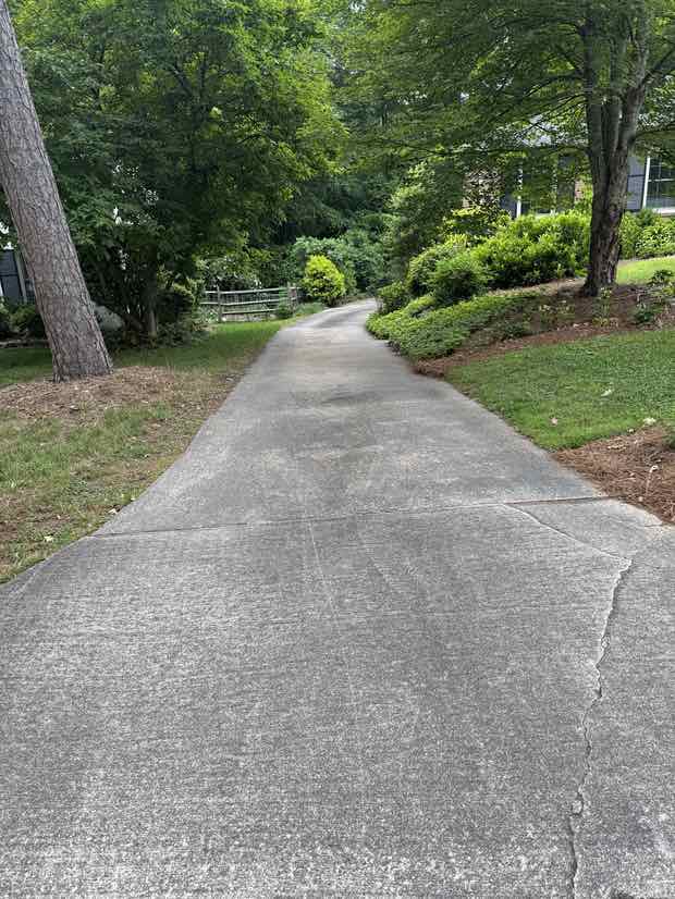A residential concrete driveway greyed and stained before pressure washing.
